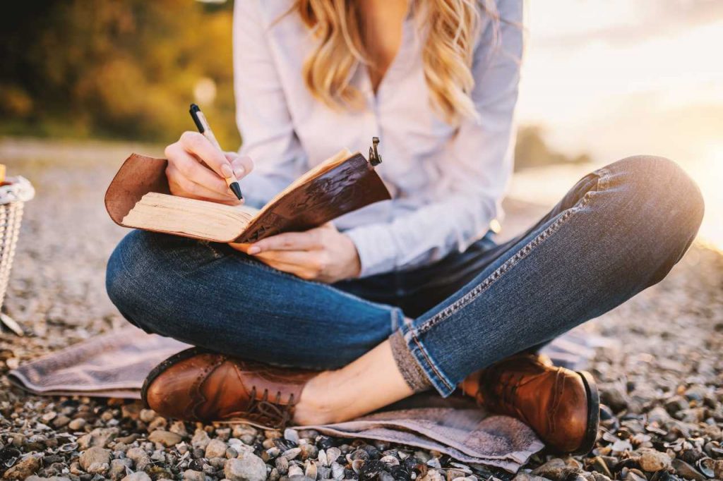 Woman sitting cross-legged on the ground writing in a book